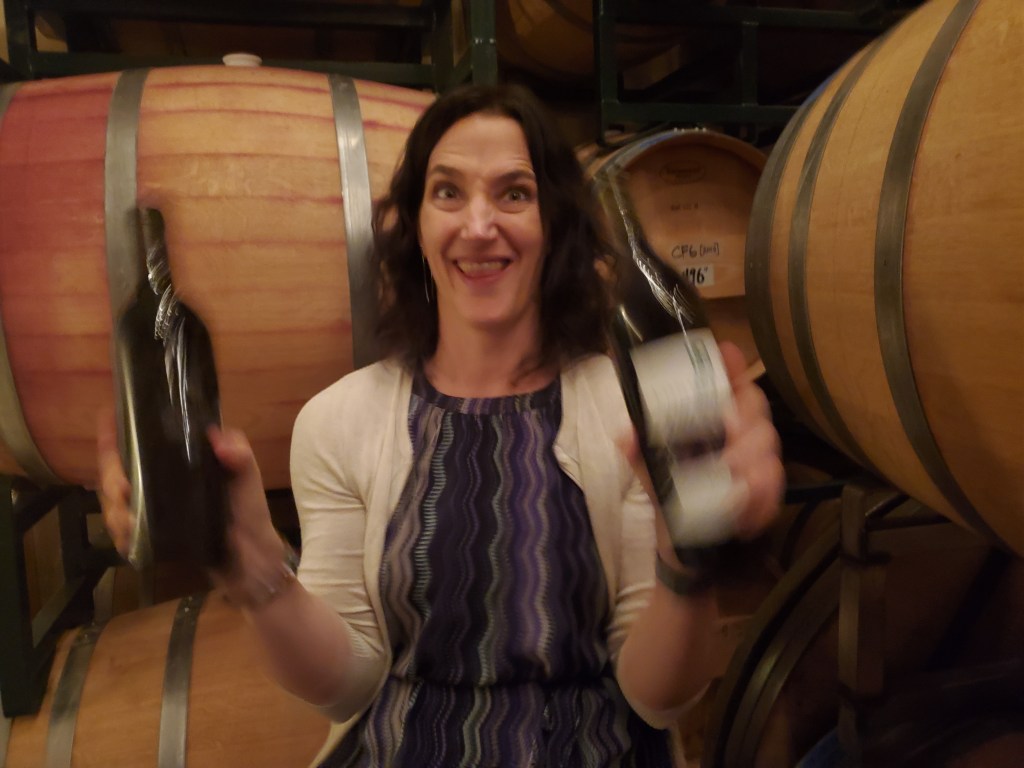 A woman with a happy grin holding 2 bottles of wine.